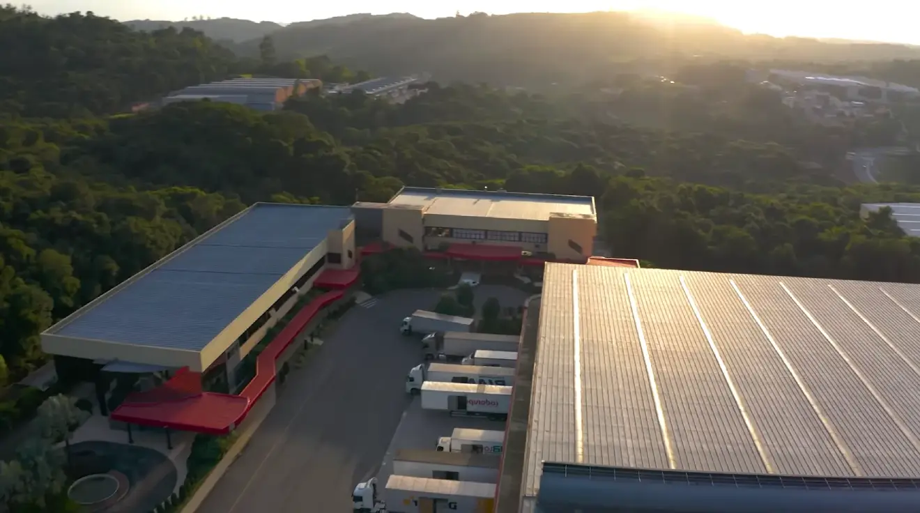 Vista aérea da fábrica Italínea, galpões industriais modernos, paleta azul-petróleo e cinza, iluminação de fim de tarde, fotografia profissional